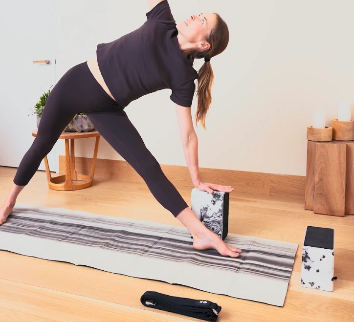 A practitioner in triangle pose on the unfolded Bento Yoga mat with a block supporting her hand