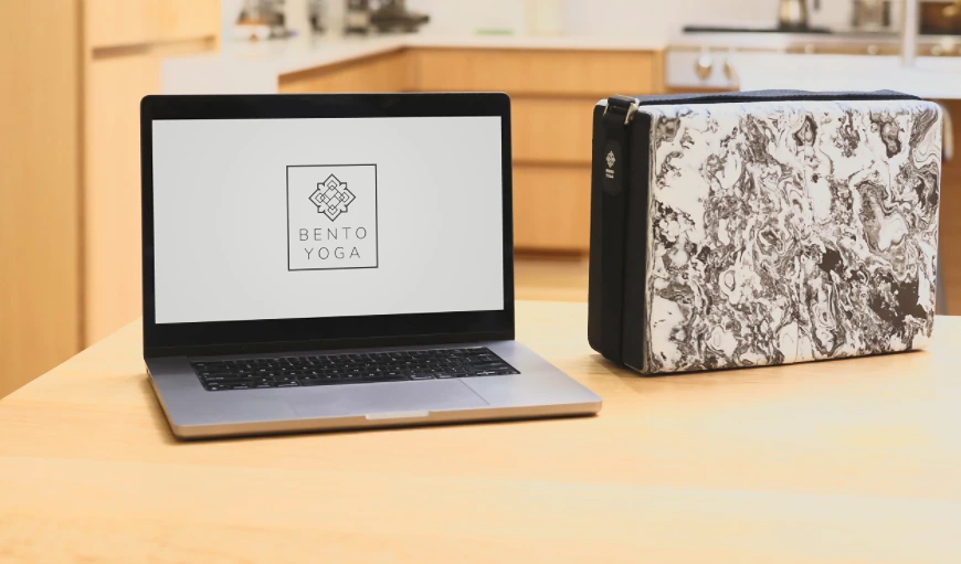 A laptop displaying Bento Yoga beside the packed ONE kit on a kitchen counter