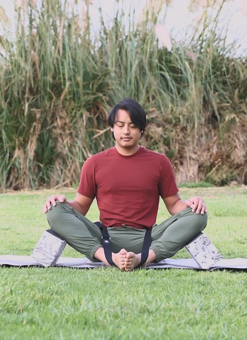 A practitioner in a seated bound-angle pose on the grass with the full Bento Yoga ONE kit
